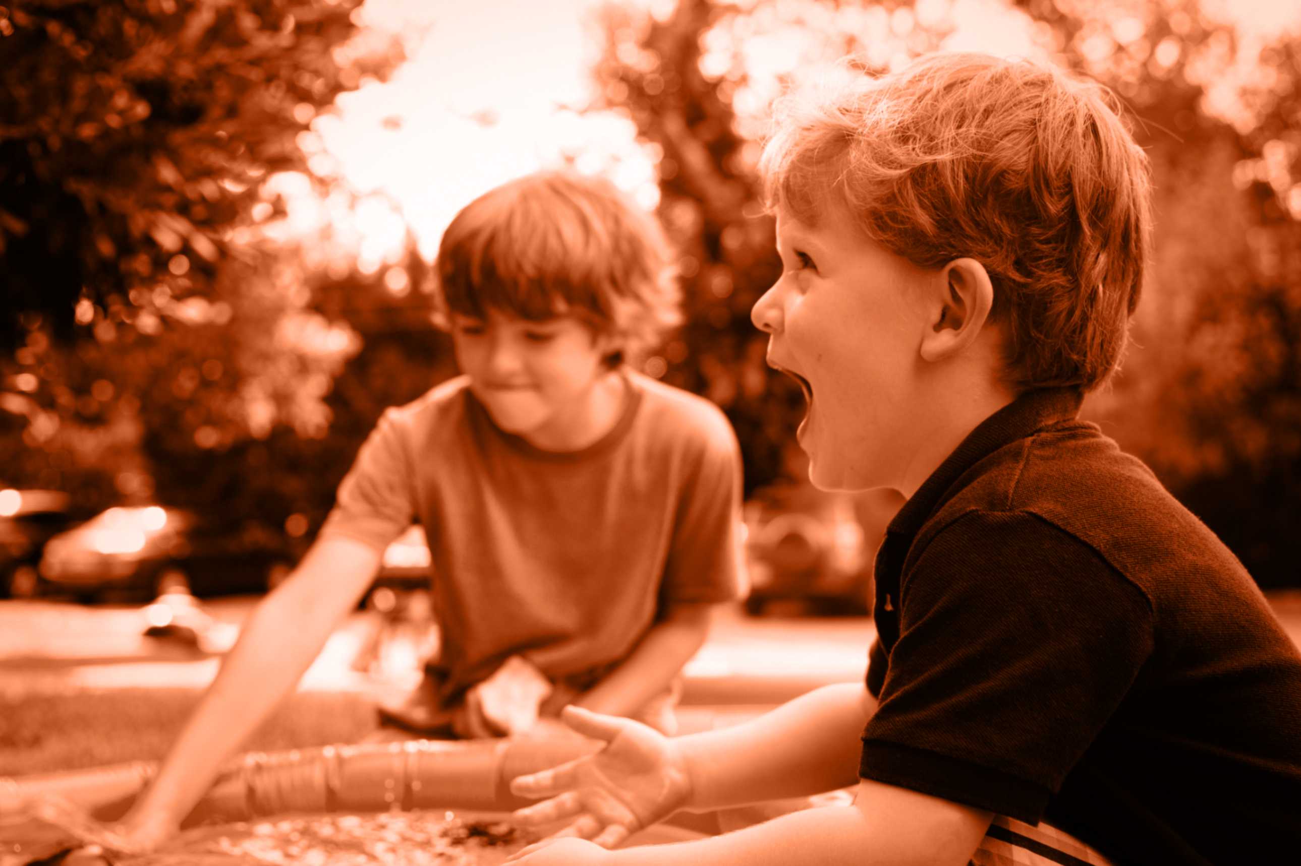 Two young boys playing outdoors near a water activity, one looking excited.