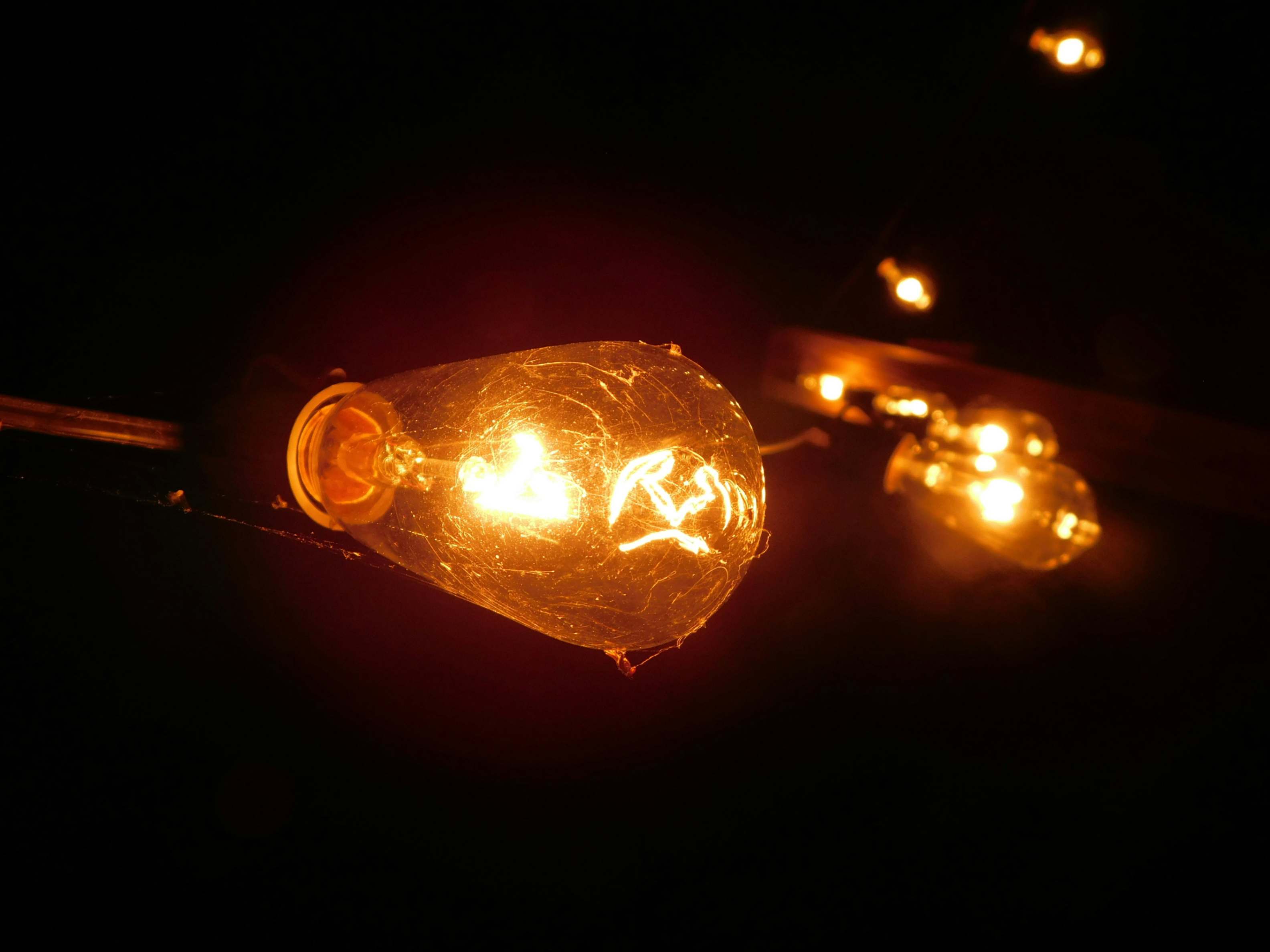 Close-up of an vintage-style light bulb with warm orange glow, sourranded by a dark background.