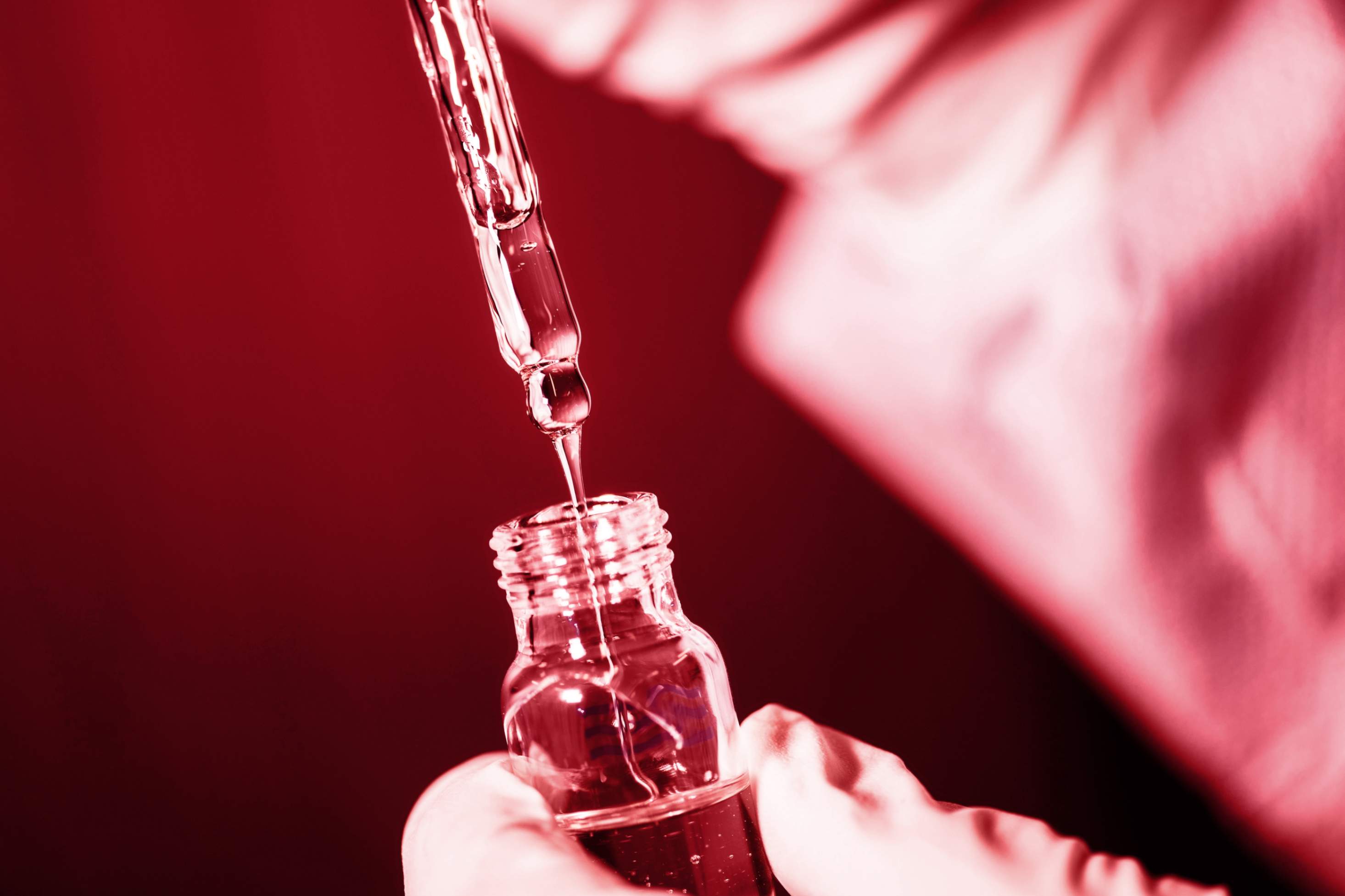 a medical dropper releasing liquid into a bottle, symbolizing medicine or laboratory work.
