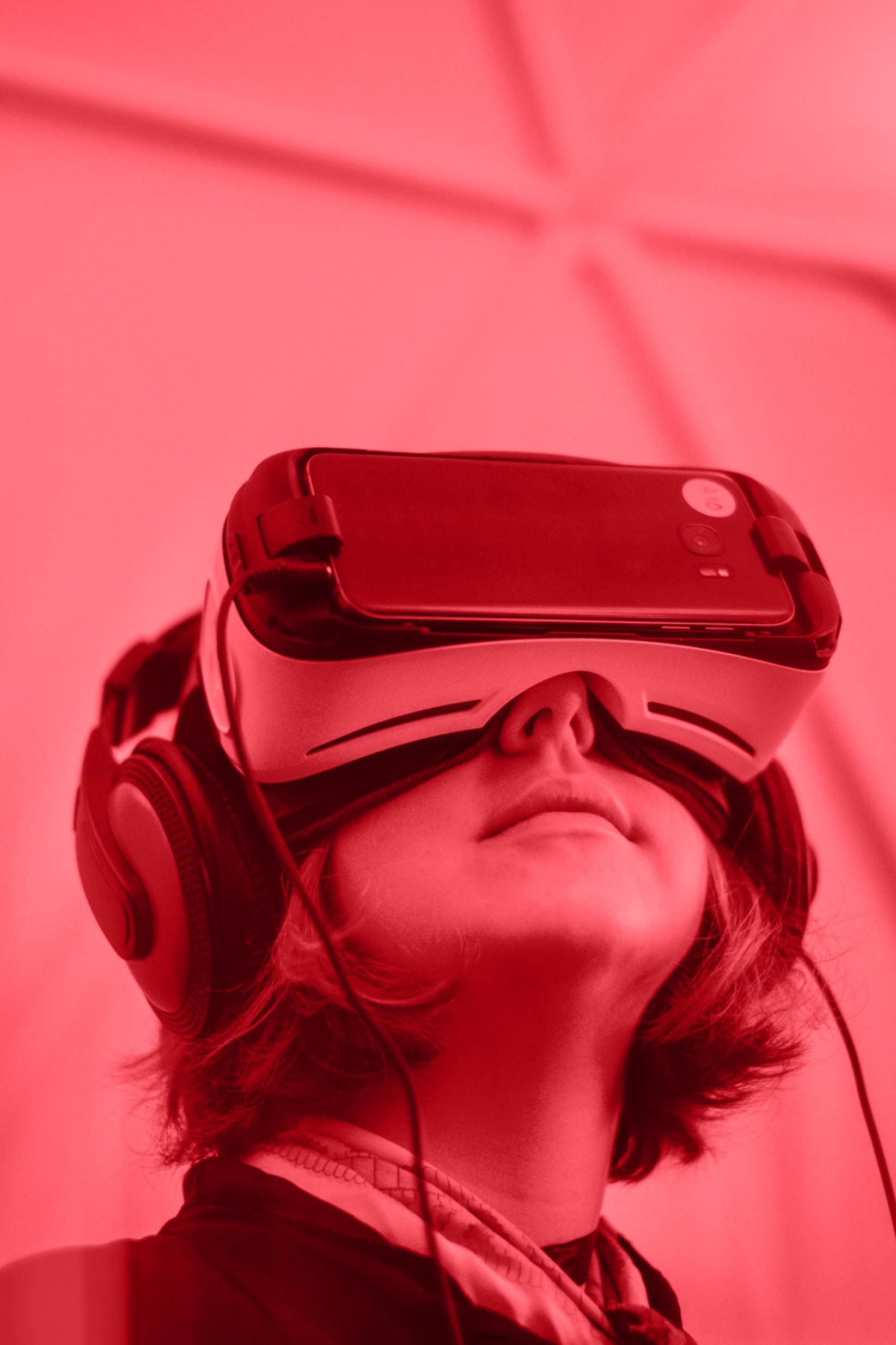 A young boy wearing virtual reality googles and headphones, looking up.