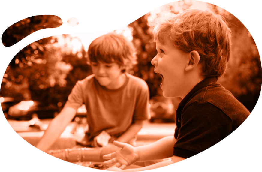 Two young boys playing outdoors near a water activity, one looking excited.
